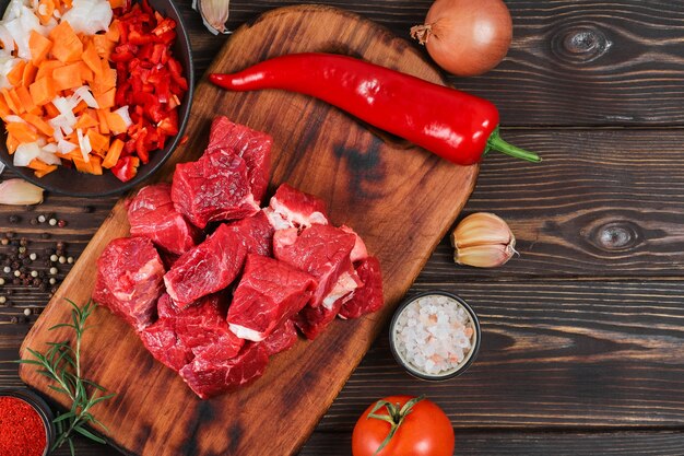 Disposición de los ingredientes para cocinar gulash o estofado. Carne de res cruda, verduras, especias, sobre mesa de madera rústica