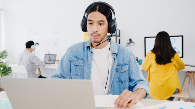 Distanciamiento social del empresario de Asia en una nueva situación normal para la prevención de virus mediante la presentación de una computadora portátil a un colega sobre el plan en la videollamada mientras trabaja en la oficina en casa. Estilo de vida después del virus corona.