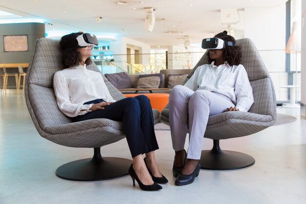 Diversas colegas femeninas con gafas de realidad virtual que hablan entre sí