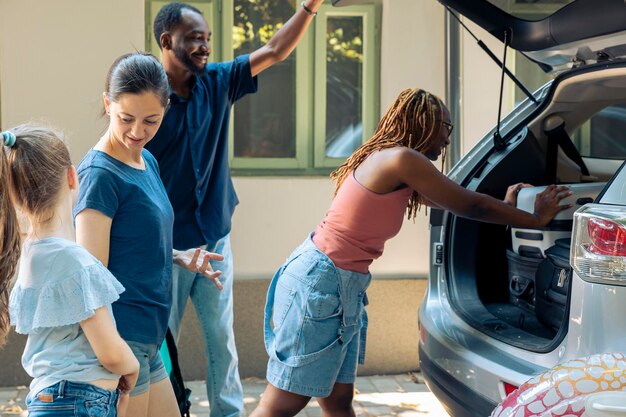 Diversas personas cargando equipaje en el maletero del automóvil, viajando en vacaciones de verano. Madre con hijo y amigos diversos poniendo maletas en el vehículo, viajando en viaje de vacaciones.