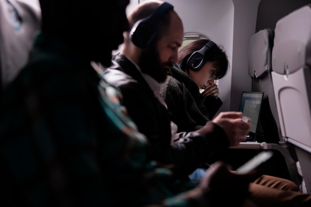 Diversas personas viajando en avión y usando laptop durante un vuelo internacional de vacaciones. Hombres y mujeres esperando llegar al destino de vacaciones, volando con servicio de vías aéreas en avión.
