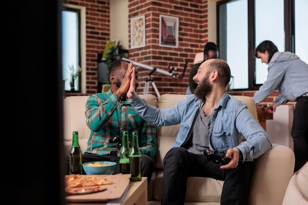 Foto gratuita diverso equipo de amigos haciendo gestos de cinco después de ganar juegos de video en la consola de televisión. celebrando la victoria de la competencia juntos en la fiesta de la casa y reuniéndonos con la gente.