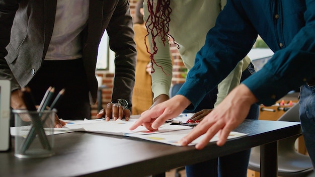 Diverso equipo de compañeros de trabajo mirando gráficos de negocios en documentos, analizando información de investigación y estadísticas sobre la revisión de diagramas. Personas que usan documentos con informes de datos infográficos. De cerca.