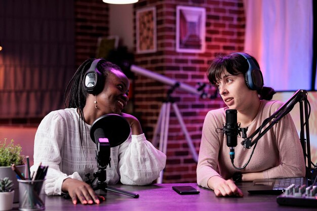 Diverso equipo de mujeres disfrutando de la conversación de podcast en el estudio, filmando vlog en línea y chateando para contenido de medios sociales. Blogueras grabando un episodio de un programa en una estación de transmisión en vivo.