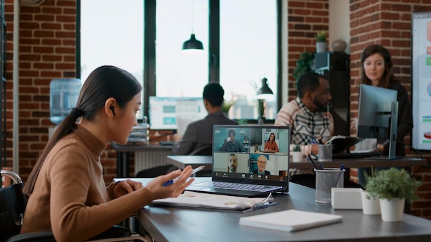 Diverso equipo de personas reunidas con mujeres en comunicación por videollamada, hablando de negocios de inicio. Empleada con discapacidad que usa videoconferencia en línea para conversación remota.