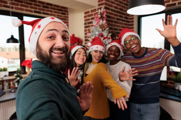 Diverso grupo de personas tomando fotos con árboles de navidad, celebrando la temporada festiva con decoraciones navideñas en la oficina de negocios. Colegas tomando fotos con adornos navideños de temporada.
