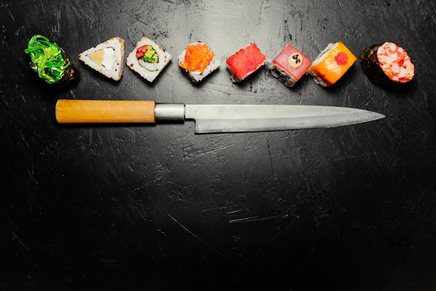 Diverso sushi con el cuchillo japonés en fondo negro de la pizarra de piedra. Sushi en una mesa.