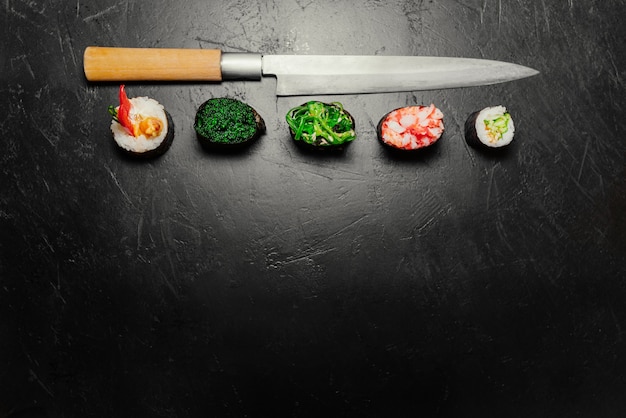 Diverso sushi con el cuchillo japonés en fondo negro de la pizarra de piedra. Sushi en una mesa.