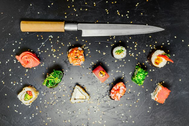 Diverso sushi con el cuchillo japonés en fondo negro de la pizarra de piedra. Sushi en una mesa.