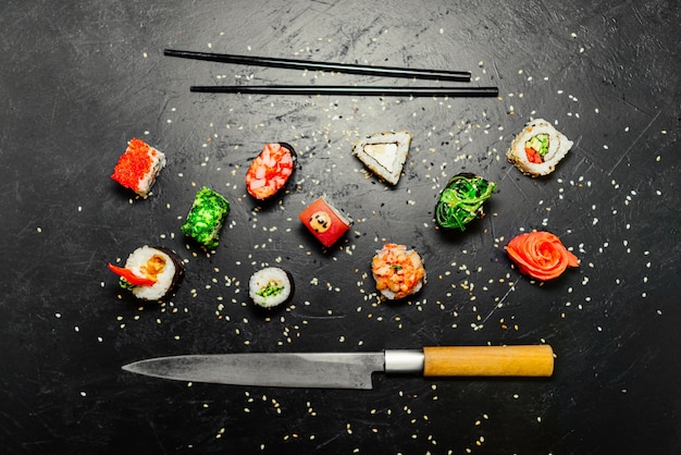 Diverso sushi con el cuchillo japonés en fondo negro de la pizarra de piedra. sushi en una mesa.