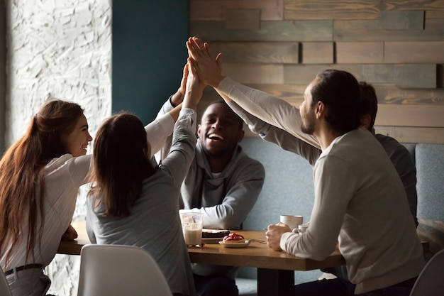Diversos amigos emocionados entregando high-five juntos en una reunión de café