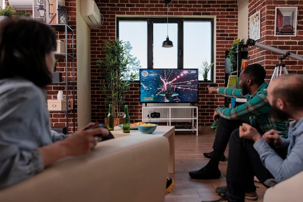 Diversos amigos que usan la consola de televisión y el joystick para jugar videojuegos, se divierten en la reunión de la casa con botellas de cerveza. Grupo de personas que disfrutan de la competencia de tiro con estrategia de juego.