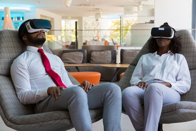 Diversos colegas en gafas de realidad virtual se relajan en el salón de la oficina
