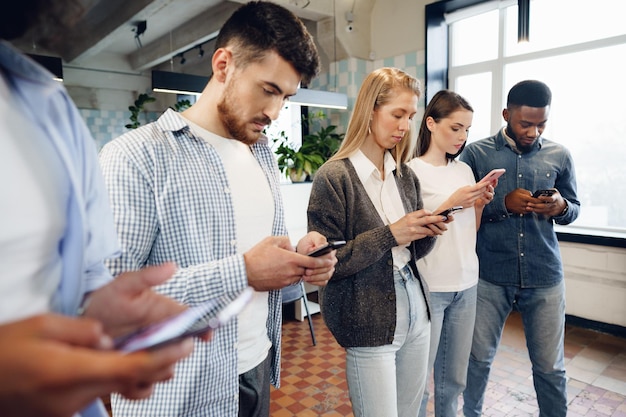 Diversos colegas jóvenes que trabajan juntos en teléfonos móviles en la oficina