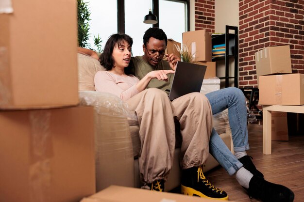 Diversos hombres y mujeres haciendo compras en línea para comprar muebles, navegando por el sitio web de Internet para inspirarse en la decoración del hogar. Mudarse juntos en un apartamento alquilado para un evento de relación.