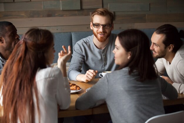 Diversos jóvenes hablando y divirtiéndose juntos en un café