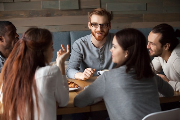 Diversos jóvenes hablando y divirtiéndose juntos en un café