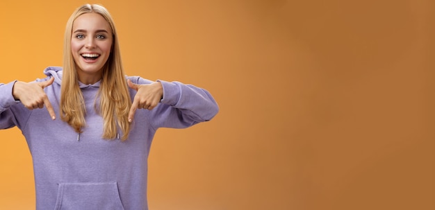 Foto gratuita divertida, alegre, bonita y rubia novia apuntando hacia abajo presente nuevo producto genial sonriendo ampliamente