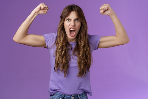 Foto gratuita divertida chica de pelo rizado levantando las manos puño bomba mostrar músculos gritando atrevidos gritos frescos alentados a ganar motivados haciendo muecas mujer fuerte y poderosa celebrando la victoria sentirse como campeona