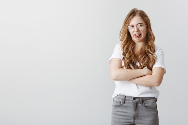 Divertida chica rubia haciendo muecas y encogiéndose de aversión, mostrando la lengua de algo repugnante