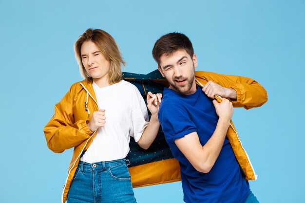 divertida joven pareja hermosa vistiendo una chaqueta sobre pared azul