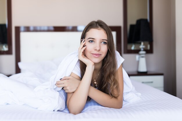 Divertida mañana feliz en la cama de una chica bonita morena, ropa de cama blanca