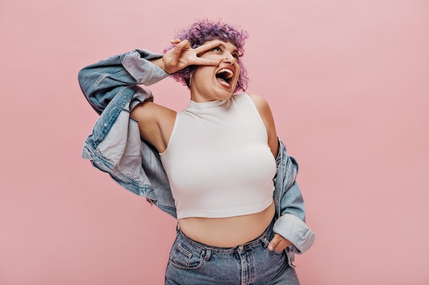 Divertida mujer adulta de pelo corto con camiseta elegante y chaqueta moderna en poses cortas y ligeras y muestra signos de paz.