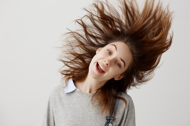 Divertida mujer vestida con suéter bromeando sacudiendo la cabeza con el pelo flotante. Amante de la música femenina alegre escuchando melodía favorita bailando divirtiéndose en la fiesta.