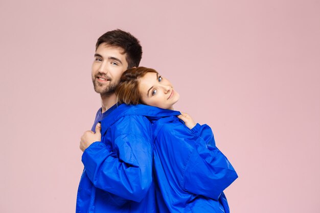 Divertida pareja hermosa joven vistiendo una chaqueta sobre pared rosa claro