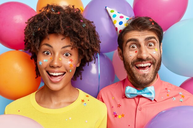Divertida pareja joven alegre posando rodeada de globos de colores de cumpleaños