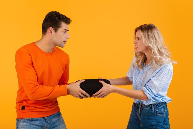 Divertida pareja joven luchando por altavoz inalámbrico escuchando música estilo colorido en naranja