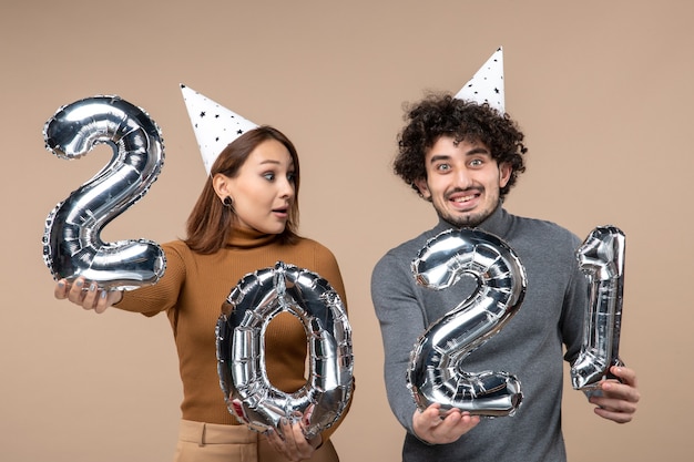 Divertida pareja joven usa poses de sombrero de año nuevo para cámara Chica mostrando y chico con y en gris