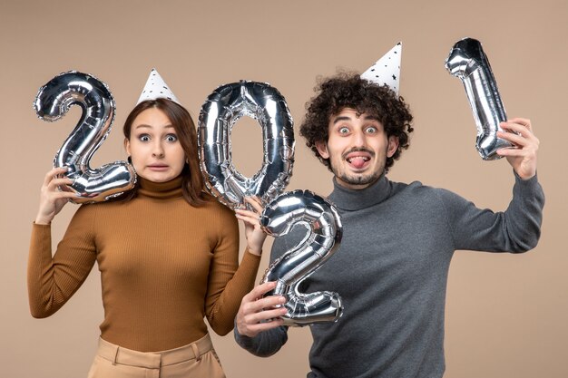 Divertida pareja joven usa sombrero de año nuevo posa para cámara Chica mostrando y chico