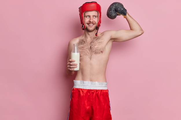 Divertido boxeador flaco masculino levanta el brazo y muestra que los músculos quieren lograr un gran resultado deportivo posa con el torso desnudo bebe leche