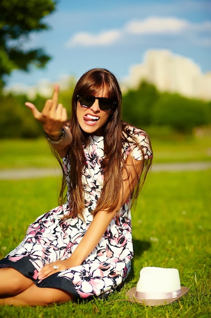 Divertido elegante sonriente hermosa joven modelo en verano brillante vestido de tela con sombrero en el parque