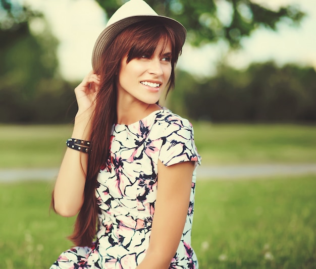 Divertido elegante sonriente hermosa joven modelo en verano brillante vestido de tela con sombrero en el parque