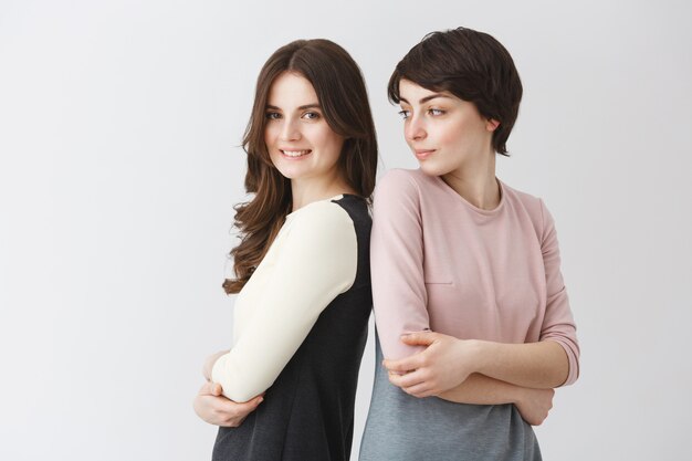 Divertido retrato de la feliz pareja de lesbianas posando juntos en trajes a juego o álbum de graduación universitaria. Chica tratando de repetir la pose de su novia para la foto.