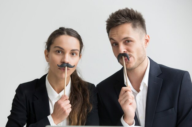 Divertidos colegas haciendo caras tontas sosteniendo bigote falso, retrato en la cabeza