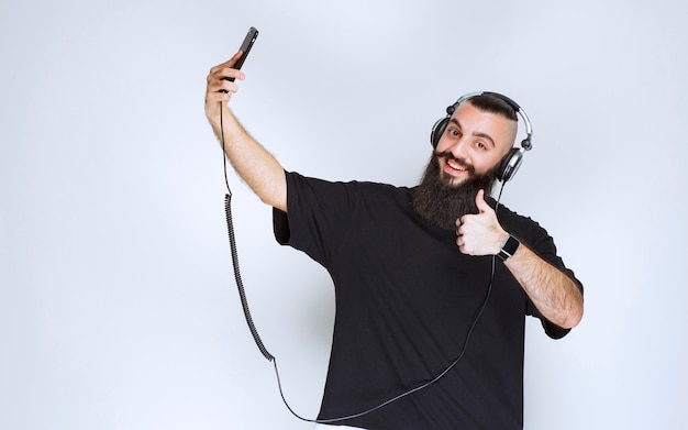 Dj con barba con auriculares abriendo la cámara del teléfono inteligente y tomando su selfie.