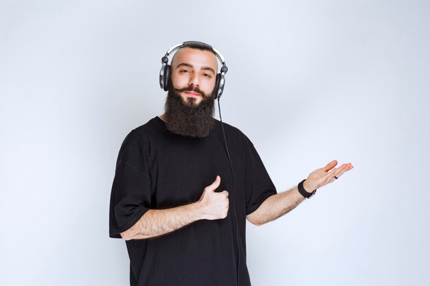 Dj con barba usando audífonos y apuntando al lado derecho.