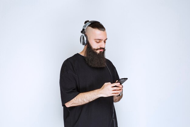 Dj con barba usando audífonos y poniendo música desde su playlist en su smartphone.