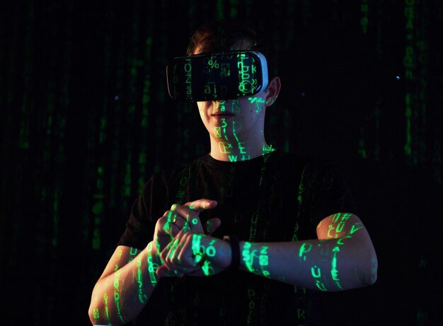 La doble exposición de un hombre caucásico y un casco de realidad virtual VR es presumiblemente un jugador o un pirata informático que descifra el código en una red o servidor seguro, con líneas de código en verde.