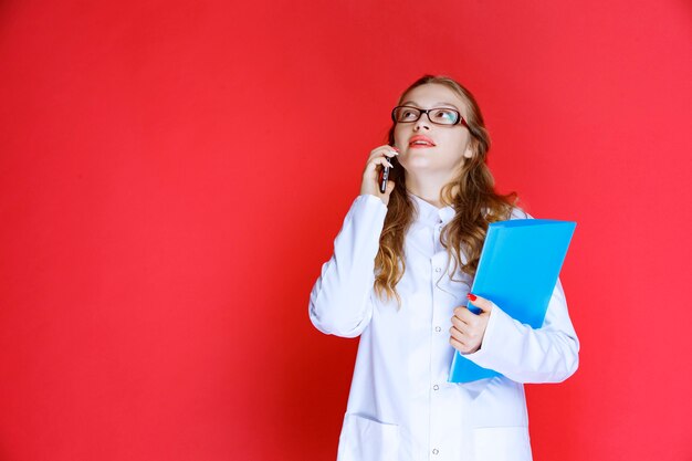 Doctor con anteojos y sosteniendo una carpeta azul hablando con el teléfono.