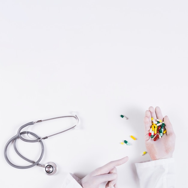 Doctor apuntando a coloridas cápsulas en la mano con estetoscopio sobre fondo blanco