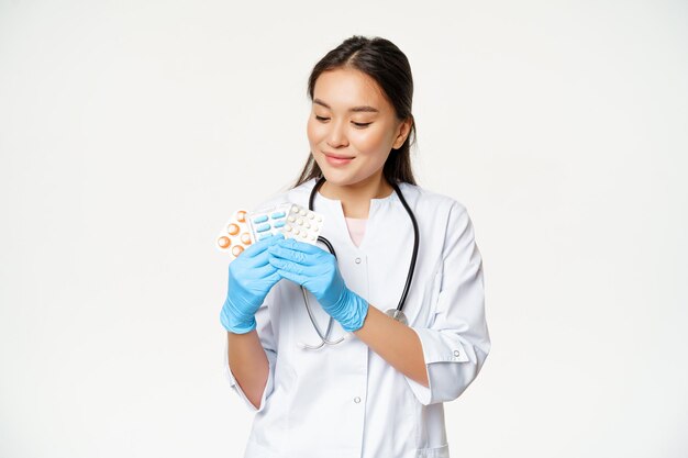 Doctor asiático sonriente mostrando píldoras médicas publicidad vitaminas sosteniendo medicamentos con guantes estériles que ...