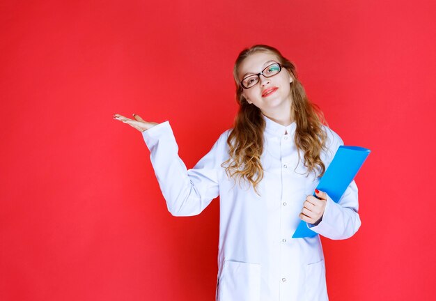 Doctor con una carpeta azul apuntando a algún lugar o alguien.