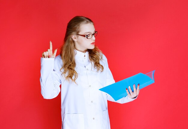 Doctor con una carpeta azul apuntando a algún lugar o alguien.