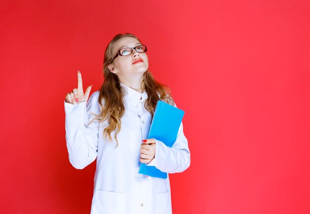 Doctor con una carpeta azul apuntando a algún lugar o alguien.