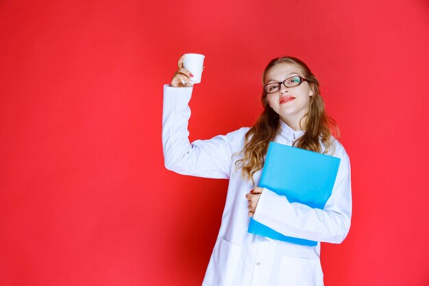 Doctor con una carpeta azul sosteniendo una taza de agua.