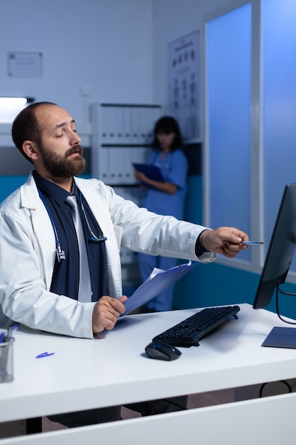 Doctor enfocado apuntando a la computadora para el trabajo de análisis en la noche